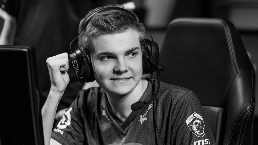 Ảnh đen trắng Cyanide mặc áo Fnatic, đeo tai nghe có micro và giơ nắm tay bên màn hình thi đấu.