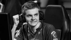 Ảnh đen trắng Cyanide mặc áo Fnatic, đeo tai nghe có micro và giơ nắm tay bên màn hình thi đấu.