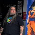 ierre mặc áo đen đứng ở cửa Micromania, cạnh hình Goku mặc võ phục màu cam.