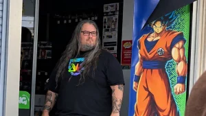 ierre mặc áo đen đứng ở cửa Micromania, cạnh hình Goku mặc võ phục màu cam.